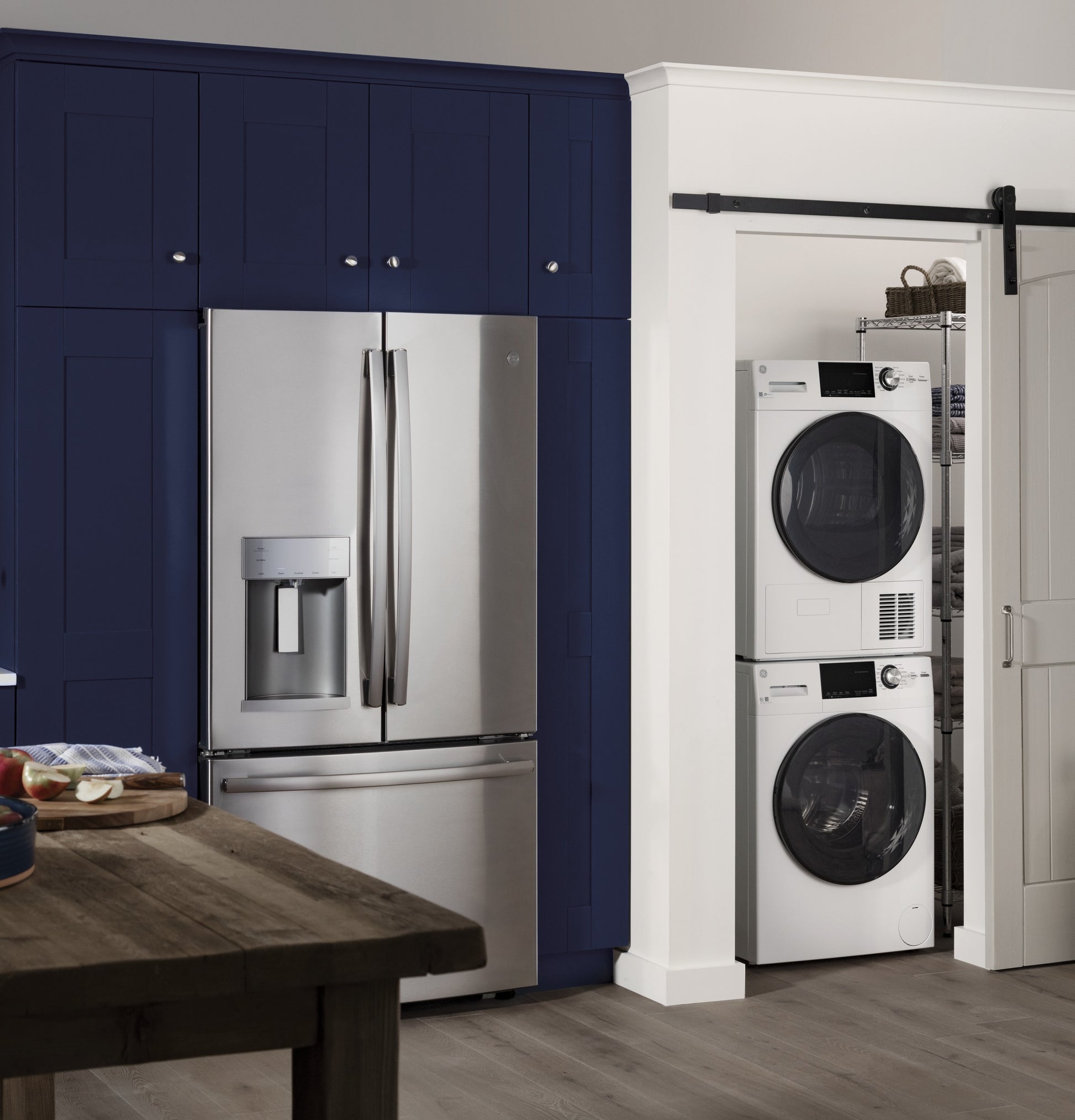 Stacked white front load washer and dryer in laundry closet next to stainless steel refrigerator in modern kitchen