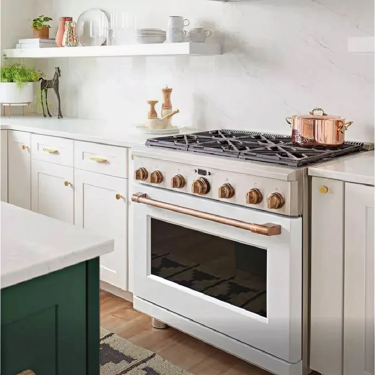 Bright kitchen corner showcasing a white gas range with brass knobs and handle, a copper pot on the stovetop, white cabinetry, and open shelves with glassware and plants.