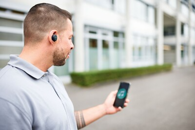 Man wearing compact black Bluetooth hearing protection earplugs using smartphone for safety and tool use outdoors