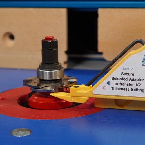 Close-up of a yellow plastic gauge tool and metal router bit on a woodworking table saw for home improvement tools