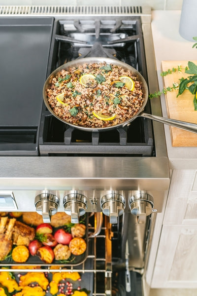 Stainless steel professional range with frying pan cooking rice and vegetables on gas burner and roasted food inside oven