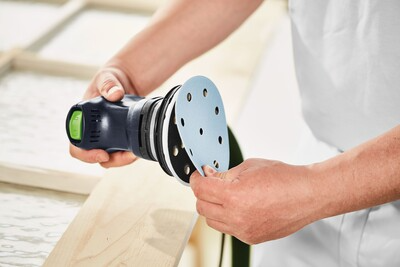 Person attaching sanding disc to Festool random orbit sander for woodworking in power tools and home improvement collections