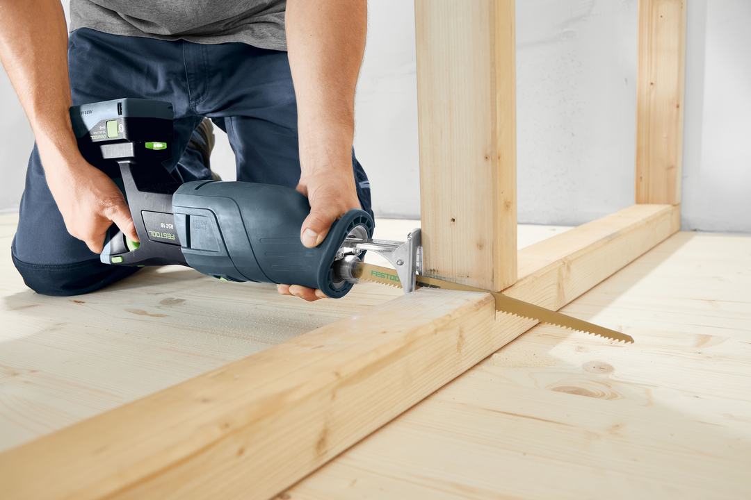 Person using Festool cordless reciprocating saw cutting wooden frame for home improvement in workshop setting