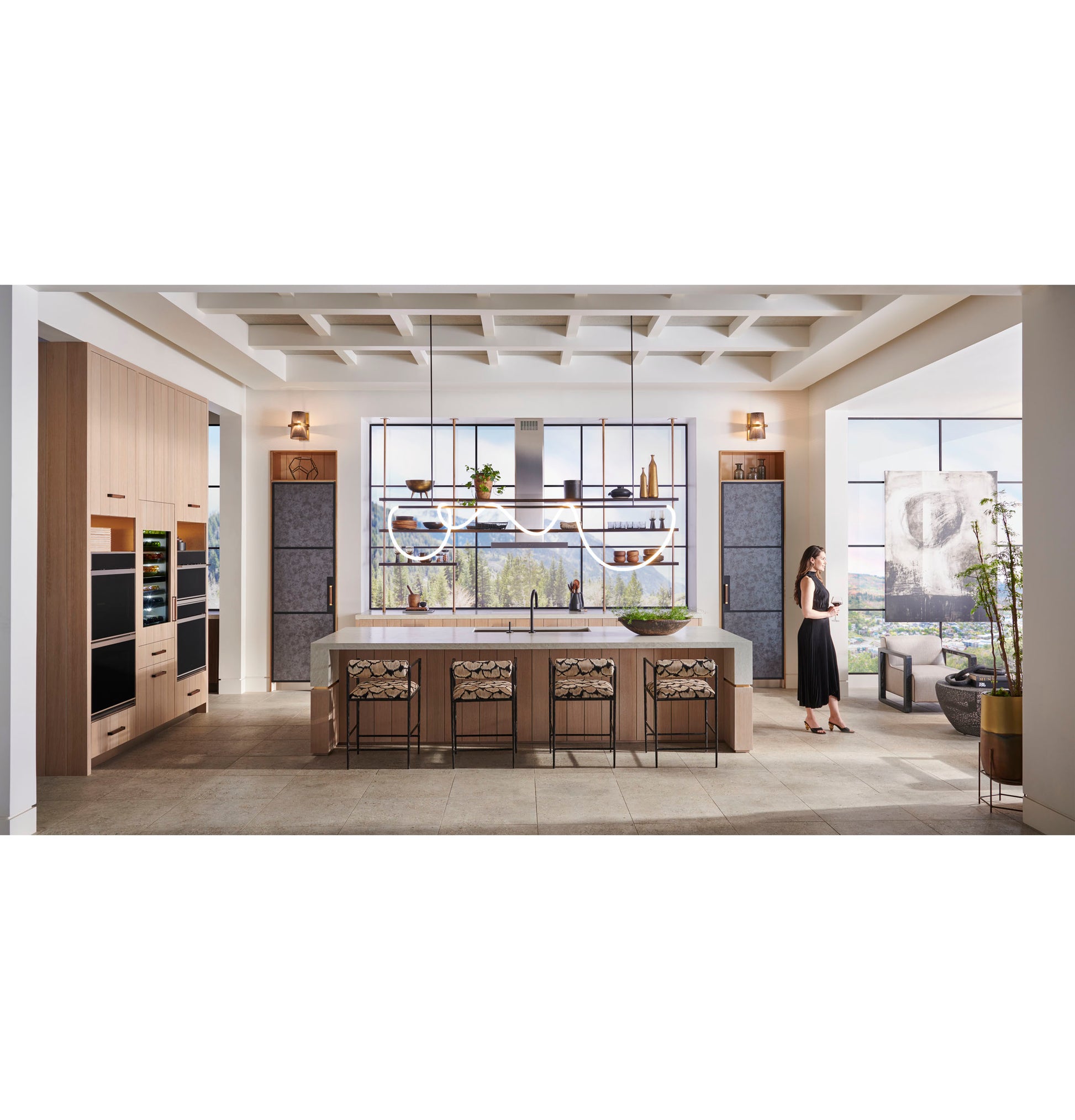 Spacious modern kitchen with wood cabinetry, illuminated minimalist double wall ovens, large island, and floor-to-ceiling windows