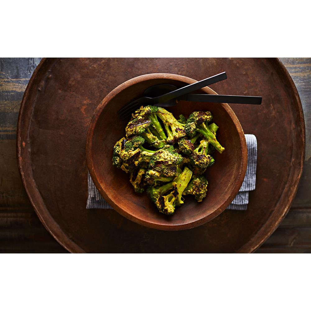 Charred broccoli florets served in a wooden bowl with black chopsticks on a rustic tray and cloth napkin