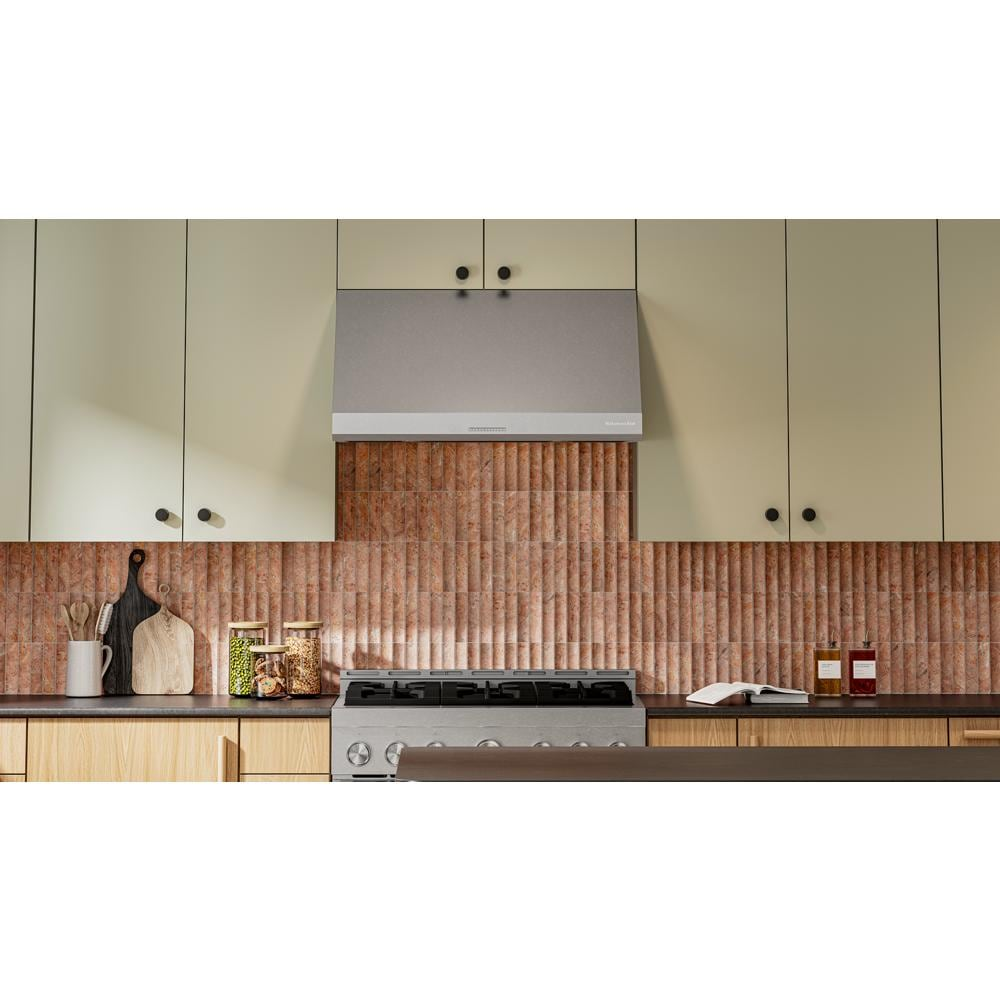 Modern kitchen scene with a stainless steel wall-mount canopy range hood above gas stove and beige cabinets