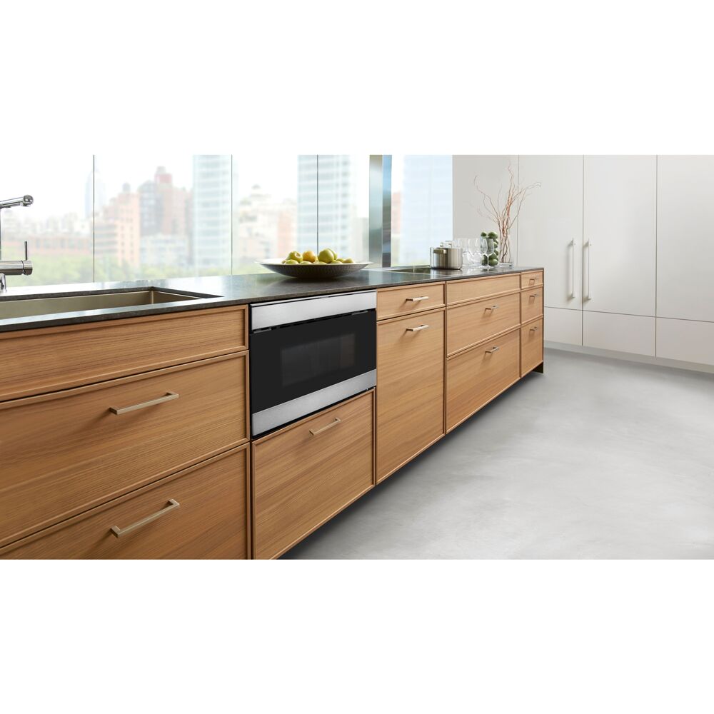 Built-in stainless steel flat panel microwave drawer installed flush with wooden lower cabinets in modern kitchen space