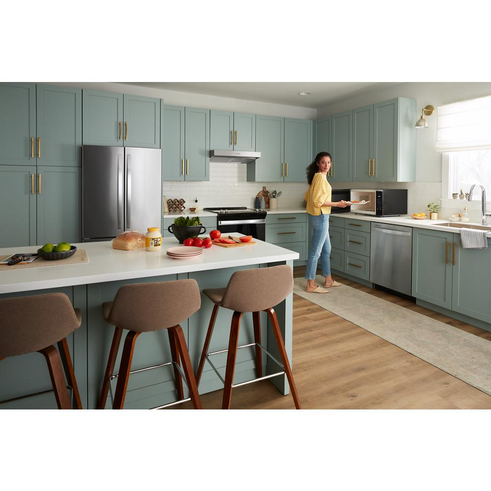 Contemporary kitchen with matte appliances, sage green cabinetry, white island countertop, and woman using microwave