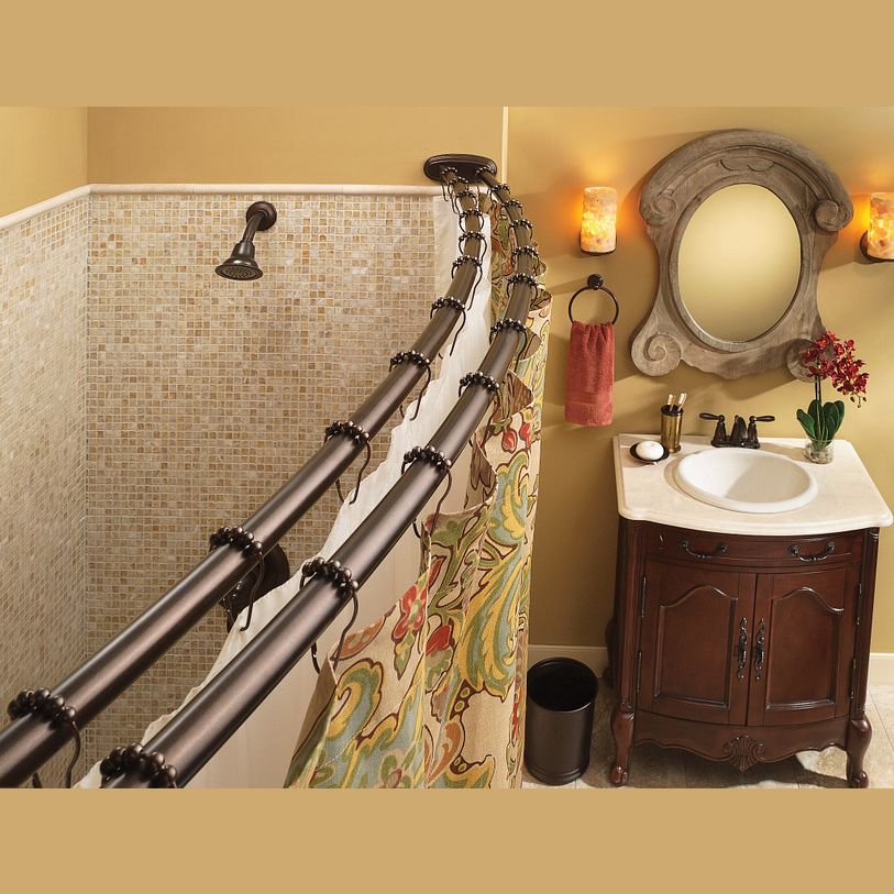 Double curved bronze shower rods with decorative hooks in a warm bathroom setting with sink and ornate mirror