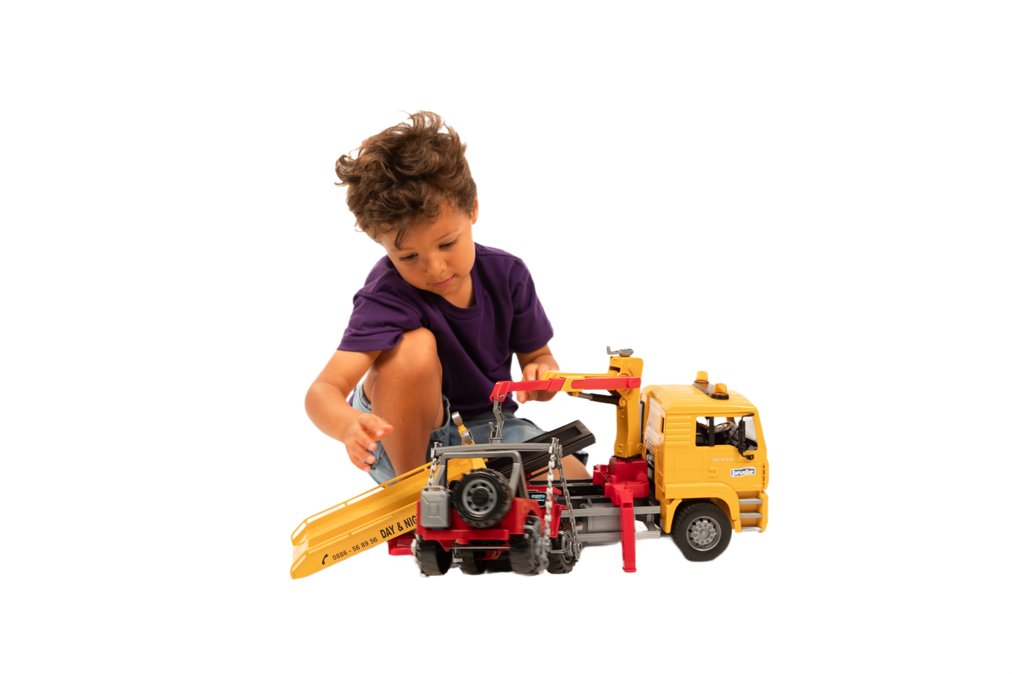 Child playing with yellow MAN TGA tow truck toy loading red cross country vehicle on ramp for imaginative play