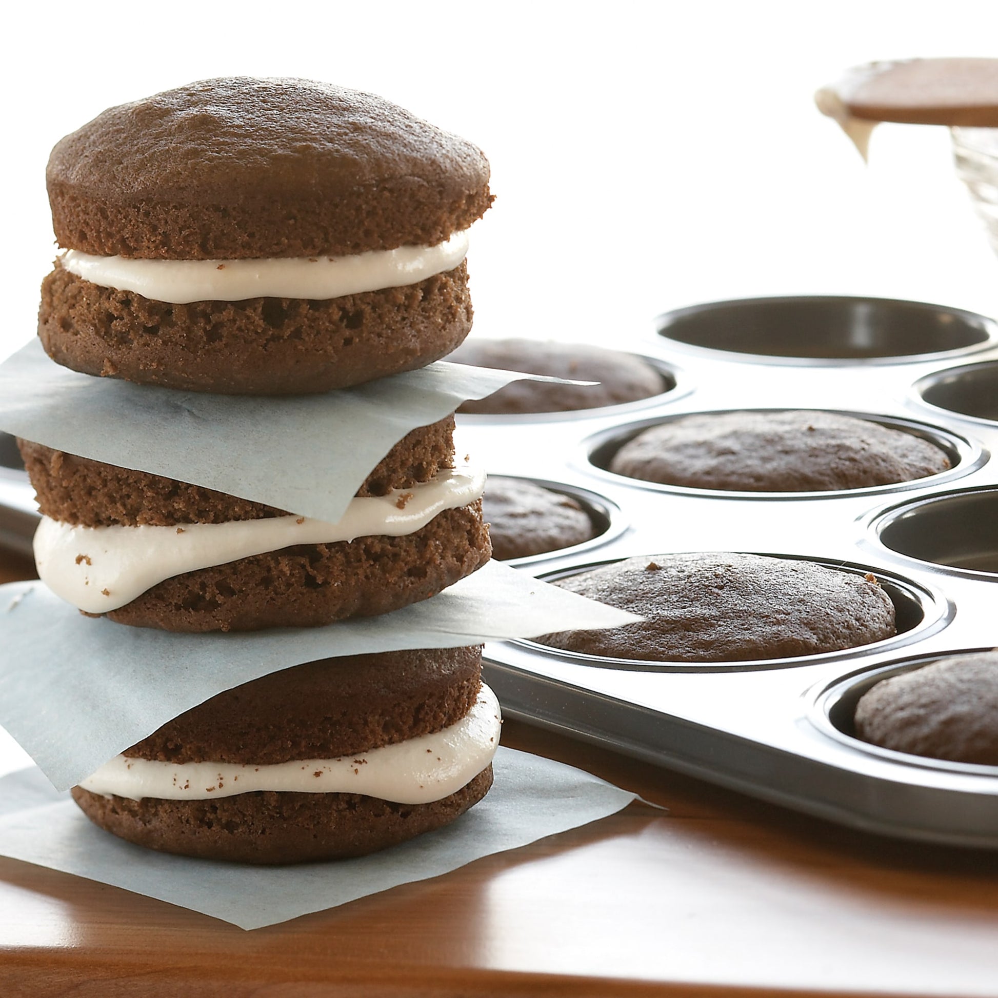 Stack of three chocolate whoopie pies with white filling beside a non-stick baking pan in kitchenware and bakeware collections