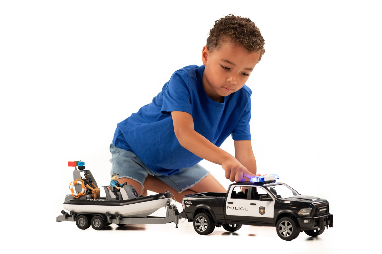 Child playing with black and white police Ram 2500 toy towing trailer with inflatable boat and two figures