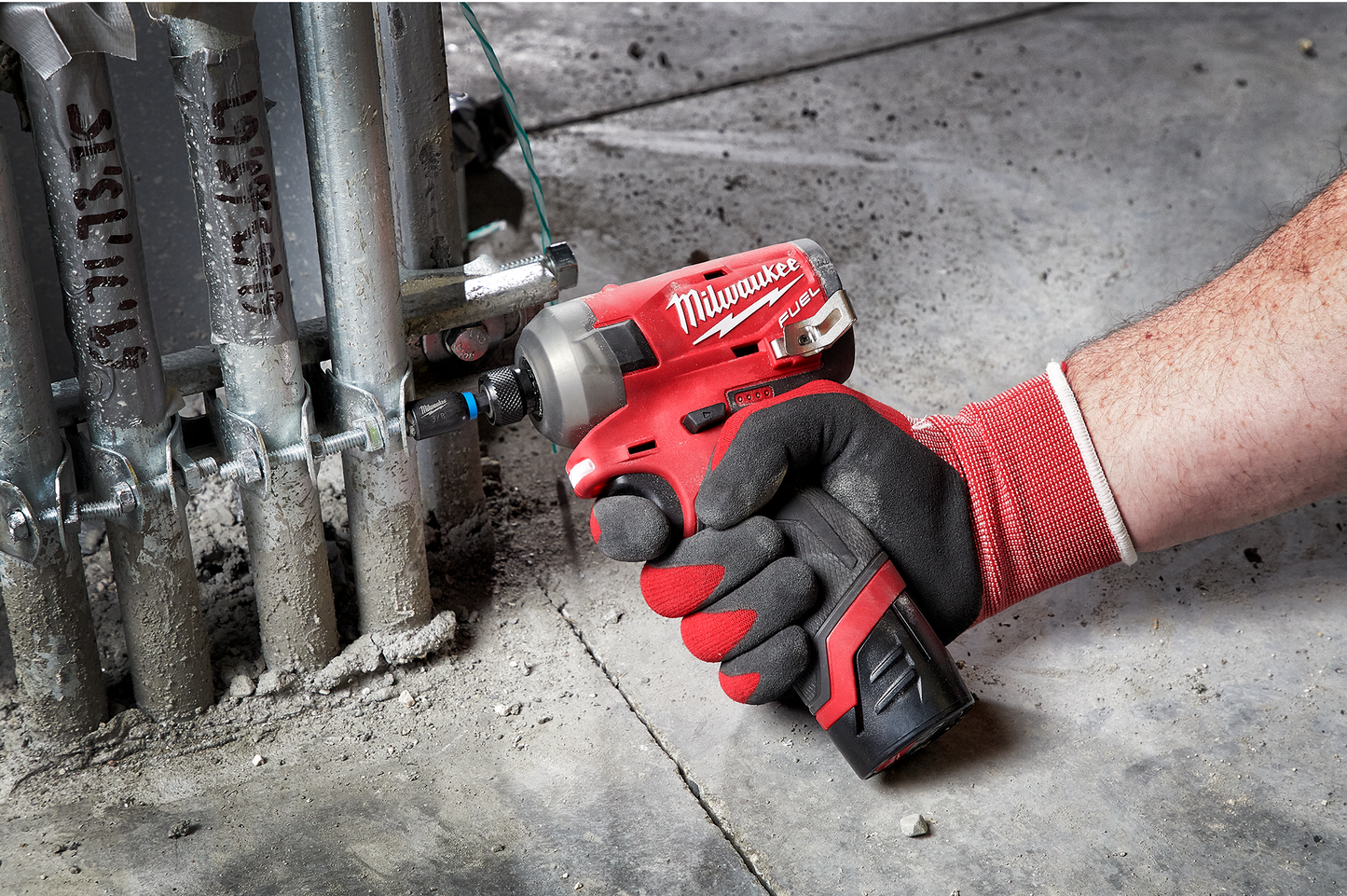 Hand wearing work glove using compact red and black Milwaukee hydraulic driver on metal conduit in home improvement setting