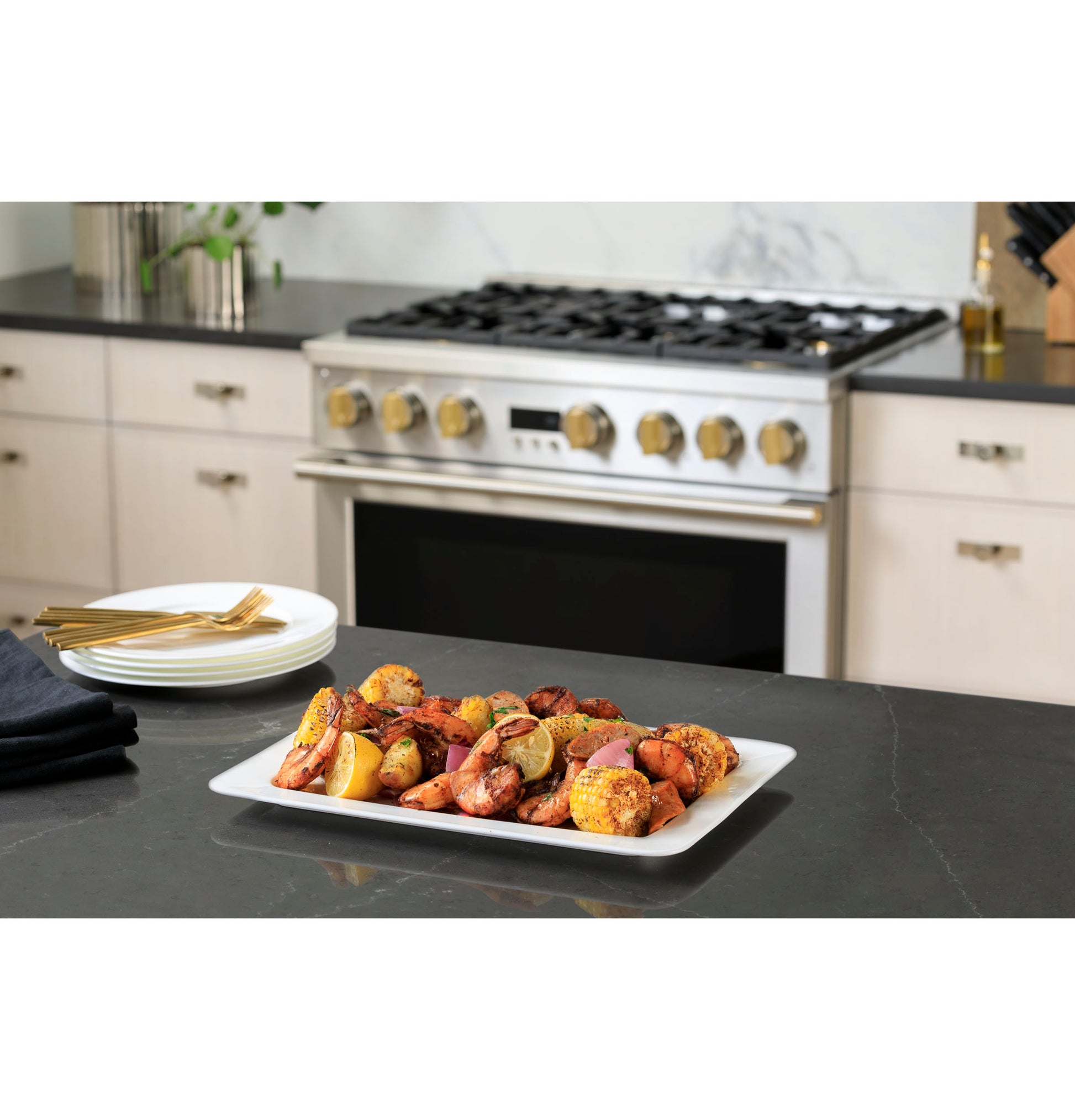Professional stainless steel gas range with four brass burner knobs in modern kitchen setting with plated seafood dish