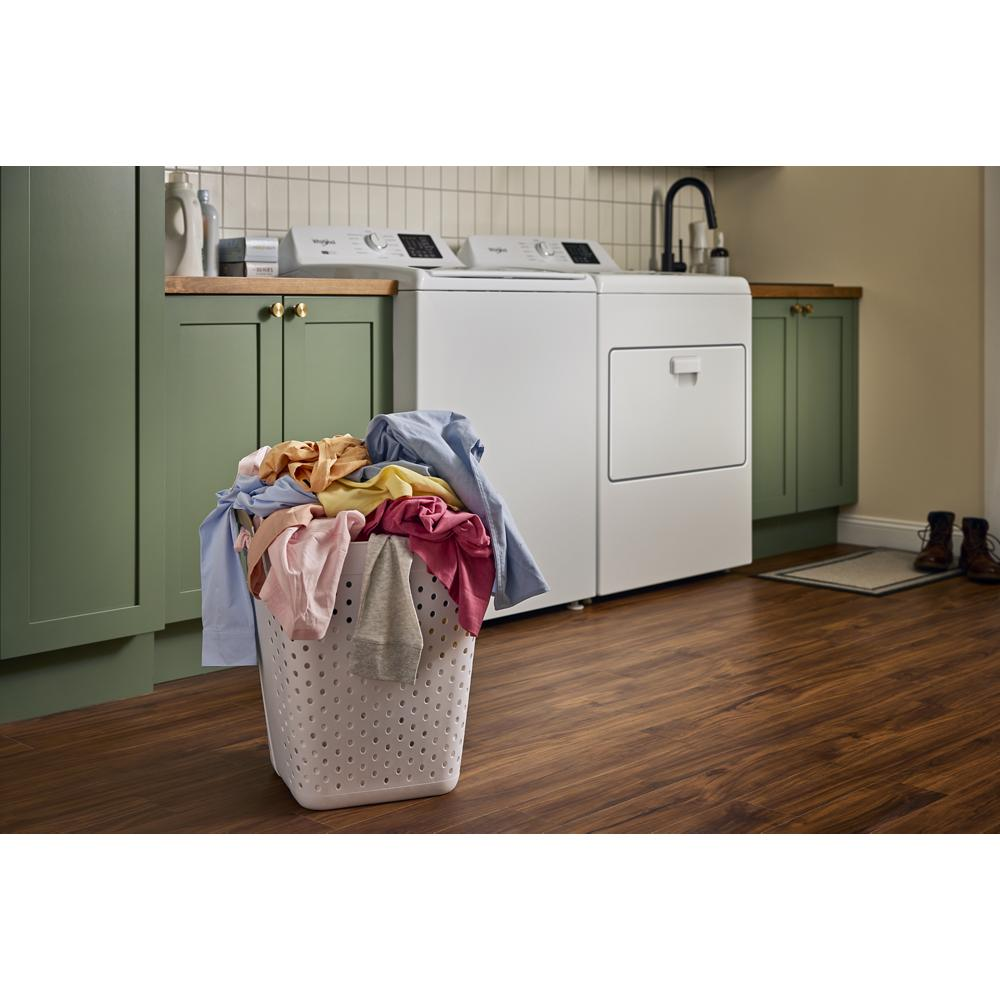 Laundry basket overflowing with colorful clothes in front of white top load washer and dryer in green kitchen-style laundry room