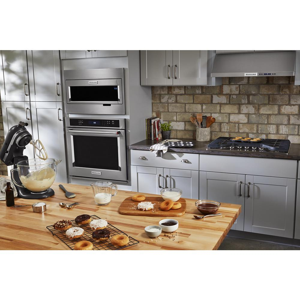 Modern kitchen featuring stainless steel oven and microwave with wooden island countertop and baking tools