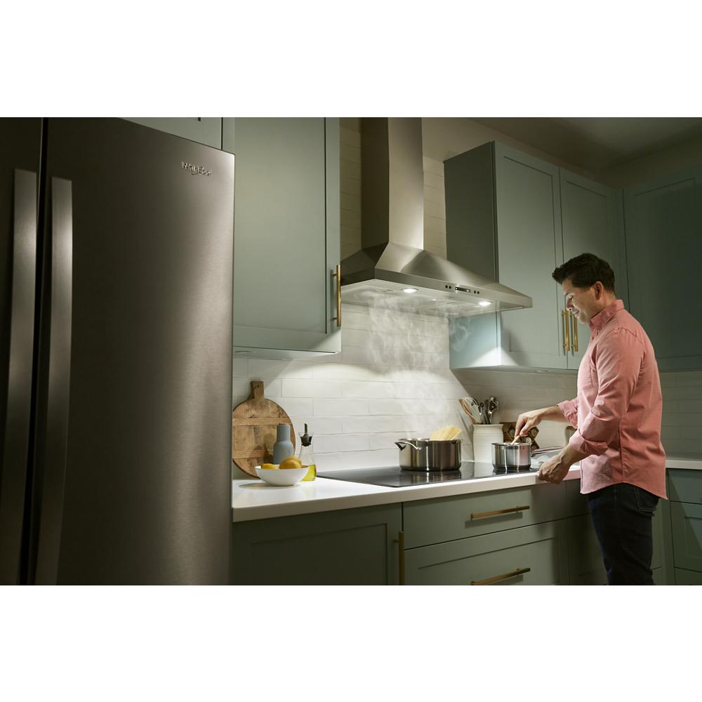 Man cooking on stove beneath stainless steel wall-mounted chimney range hood in modern kitchen setting