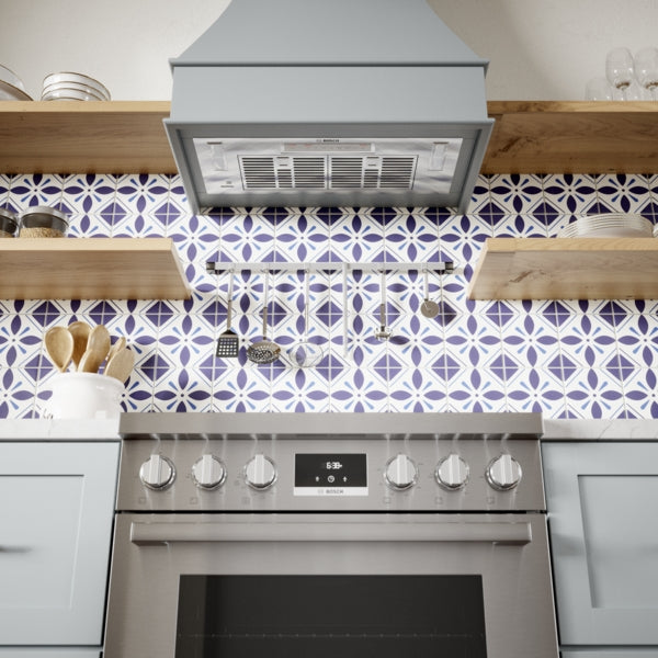 Modern kitchen setup with stainless steel range and gray custom insert hood above patterned tile backsplash