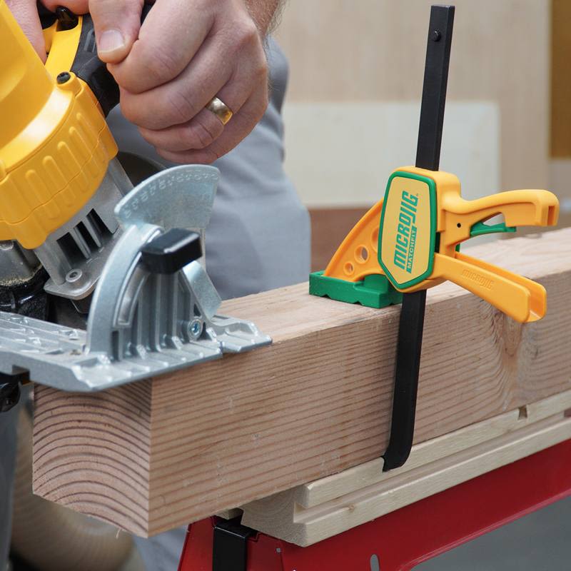 Yellow and green quick-release clamp securing wood while cutting with circular saw in tool and saw accessories collections