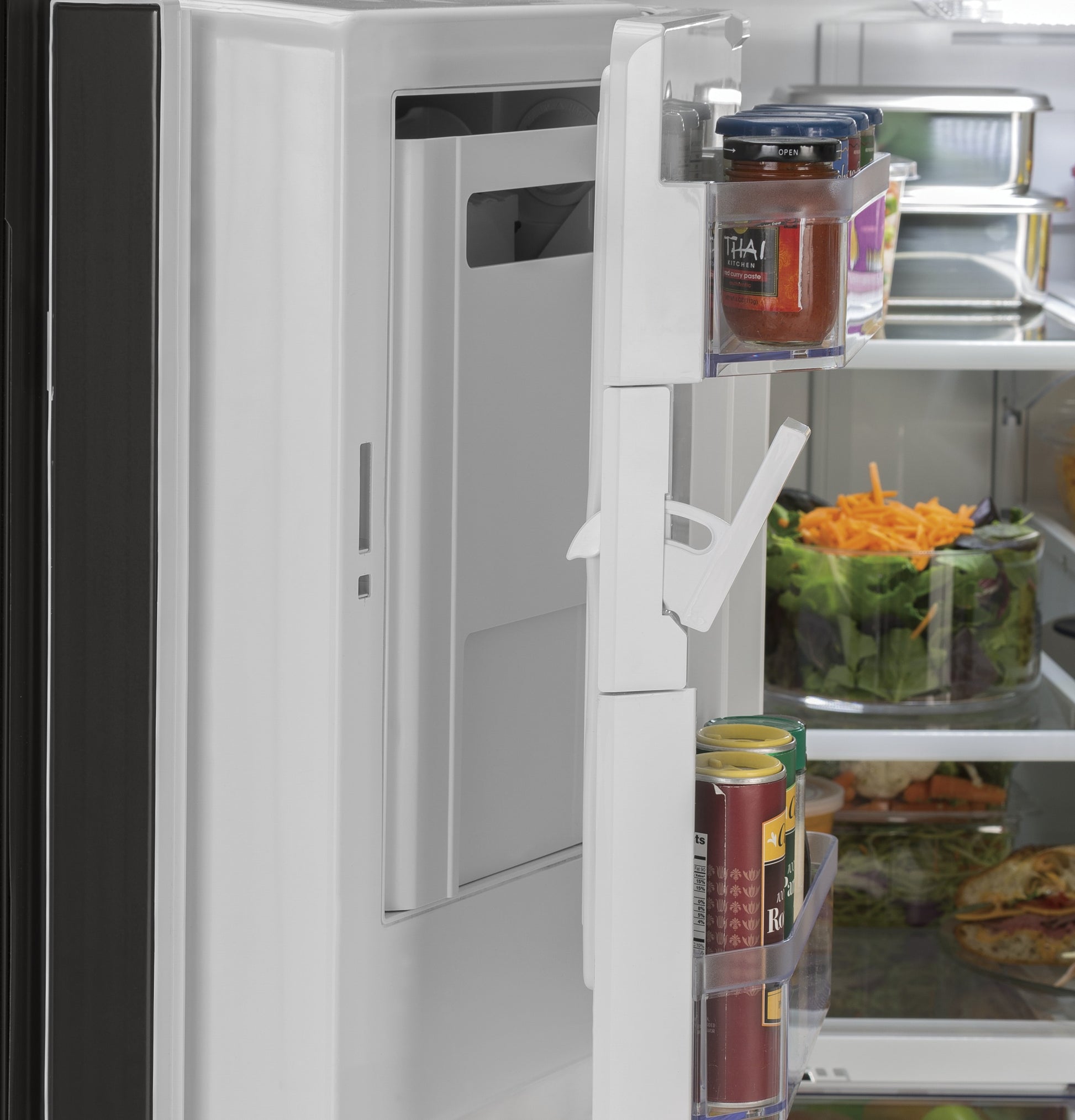 Door shelves inside open stainless steel refrigerator with organized jars, canned goods, and fresh salad in interior compartments