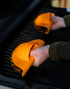 Orange silicone grill mitts offering heat protection while handling food on outdoor grill in grilling accessories collection