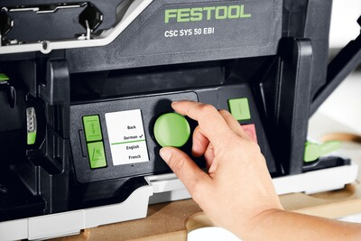 Hand adjusting a green control knob on a compact Festool cordless table saw in a woodshop setting