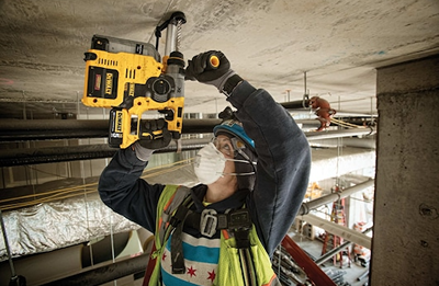 Construction worker using a yellow cordless rotary hammer drill on a concrete ceiling for home improvement tasks