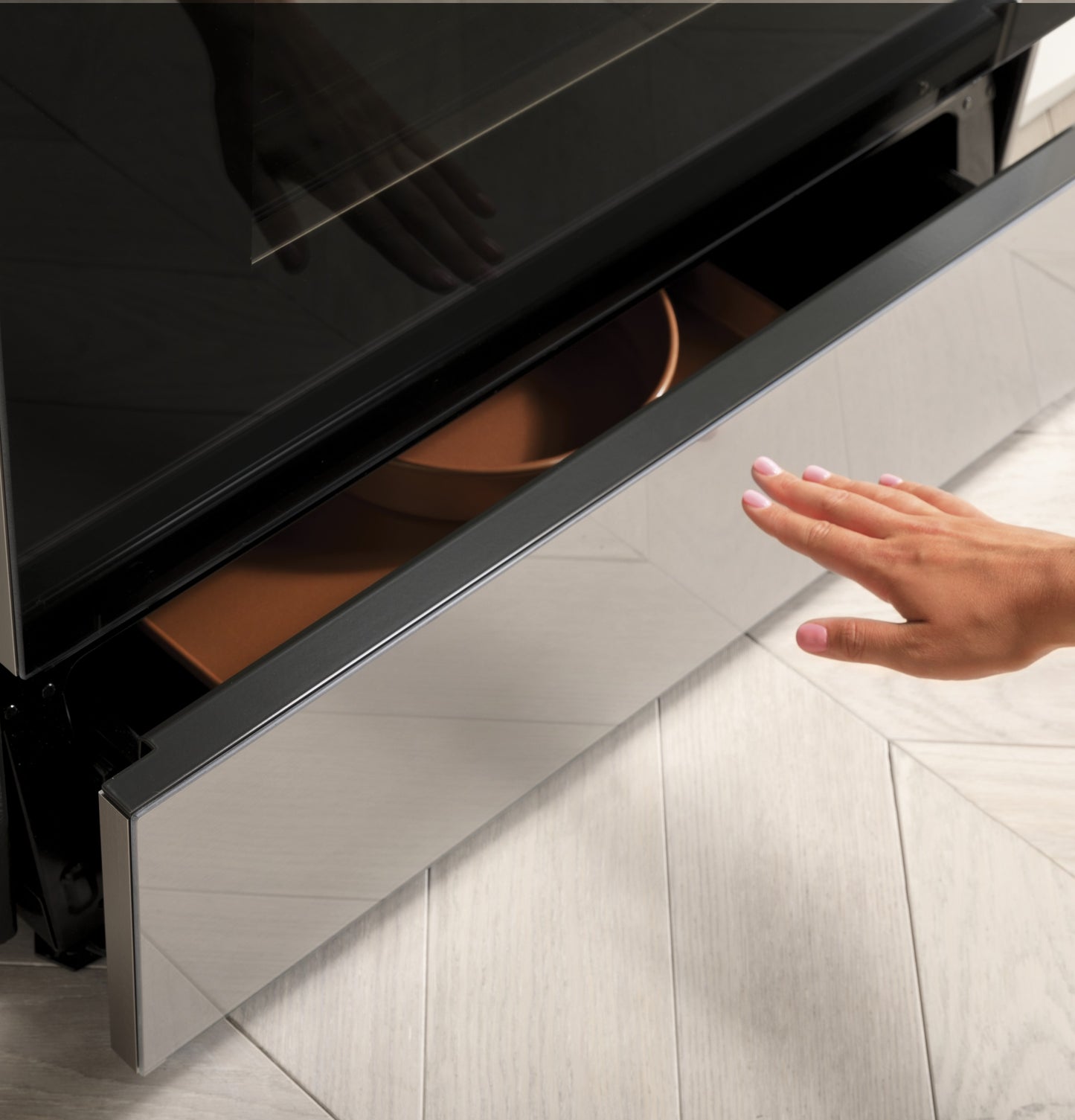 Hand reaching to open sleek platinum glass drawer of smart slide-in range in modern kitchen setting