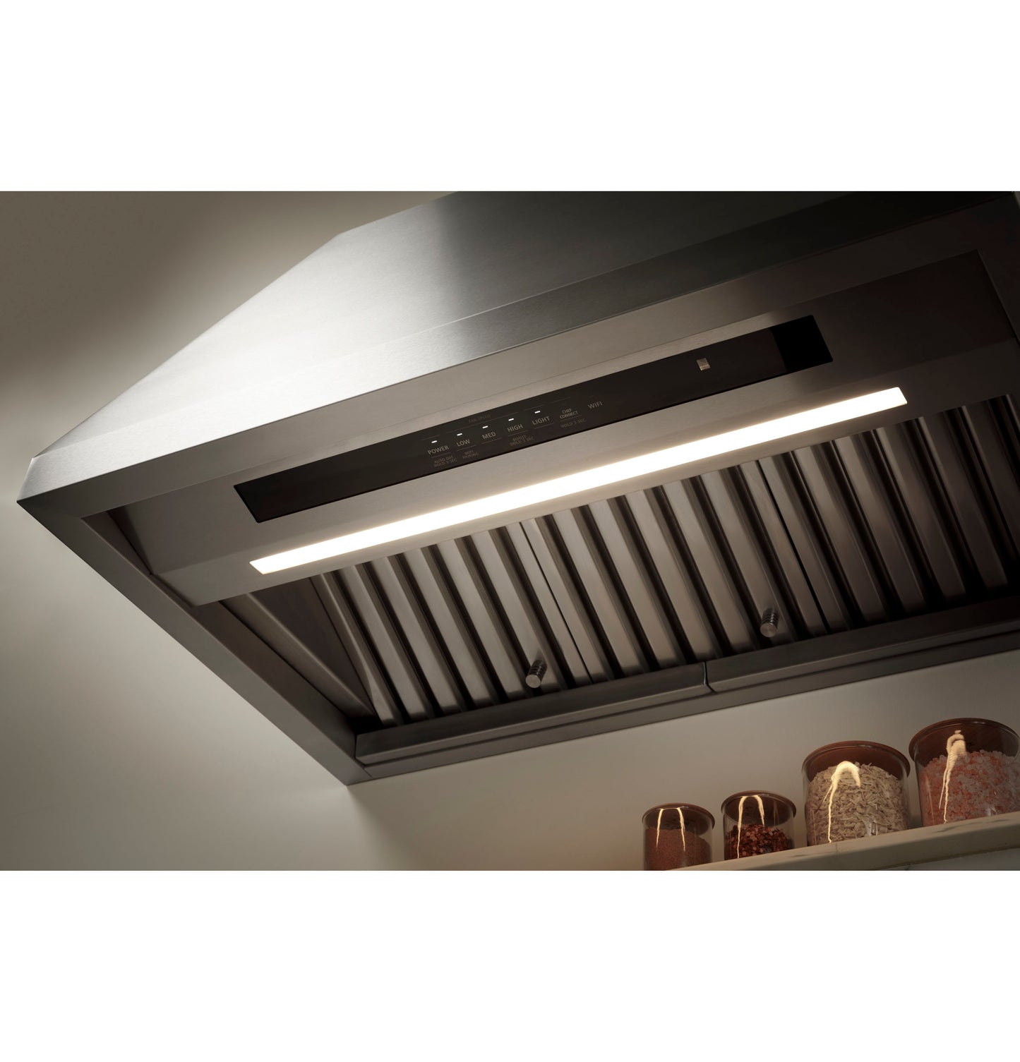 Close-up of modern stainless steel range hood with built-in light and metal baffle filters in kitchen appliances setting