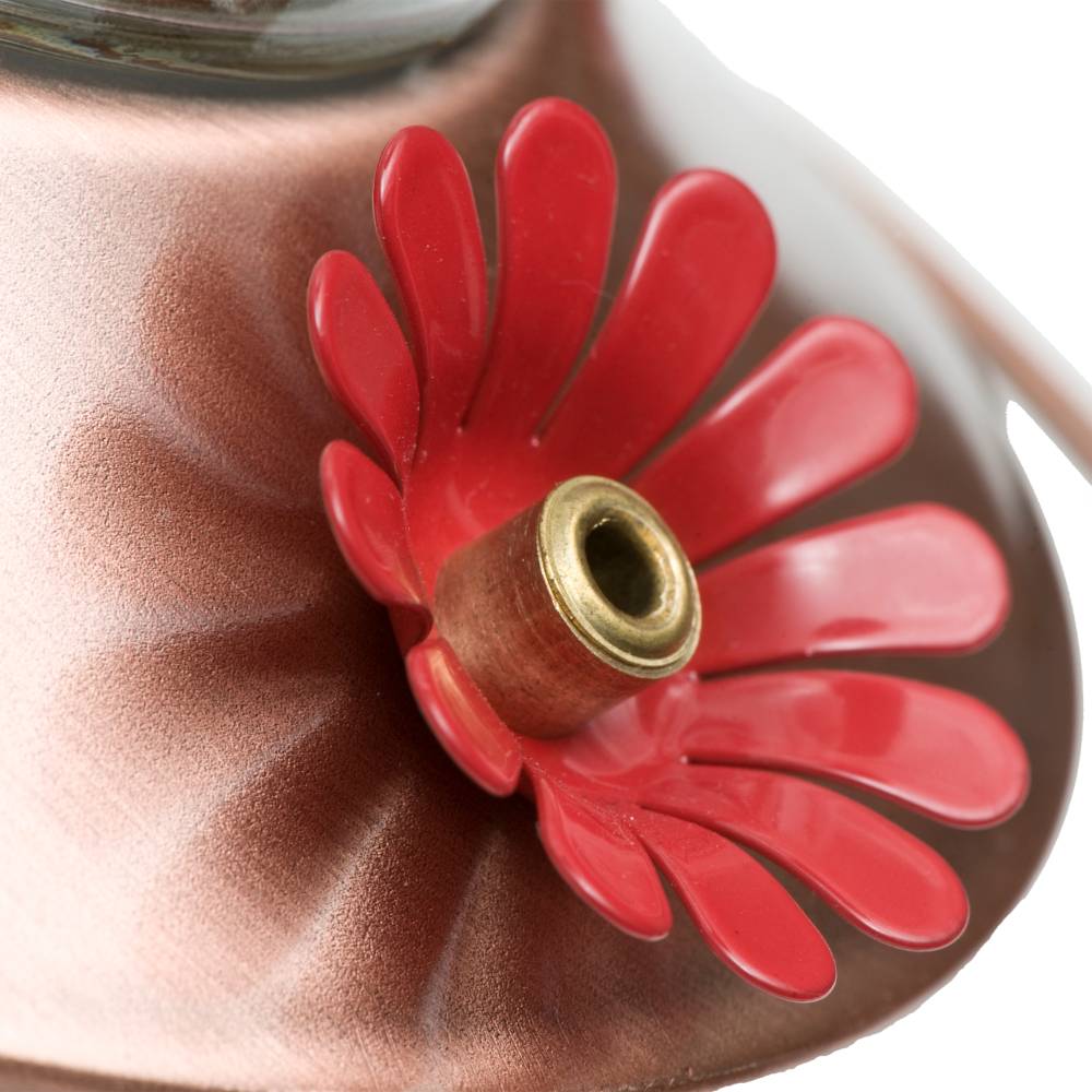 Close-up of a copper-toned hummingbird feeder with a red flower-shaped feeding port and brass center ring.