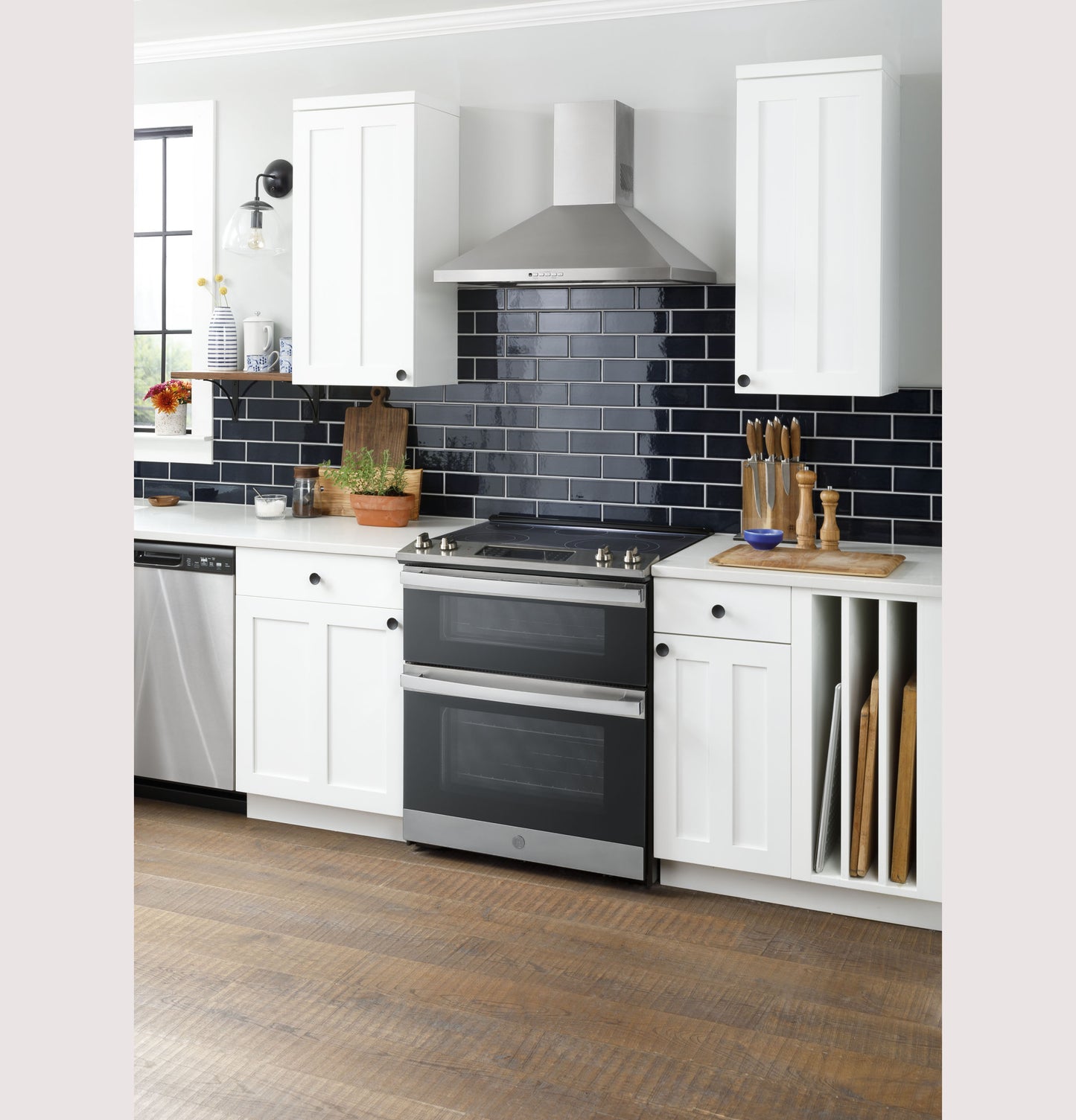 Modern kitchen setup with white cabinetry, black subway tile backsplash, and stainless steel double oven range and hood