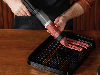Person using clear and black jerky gun to shape ground meat on black drying rack for kitchenware collections under $50
