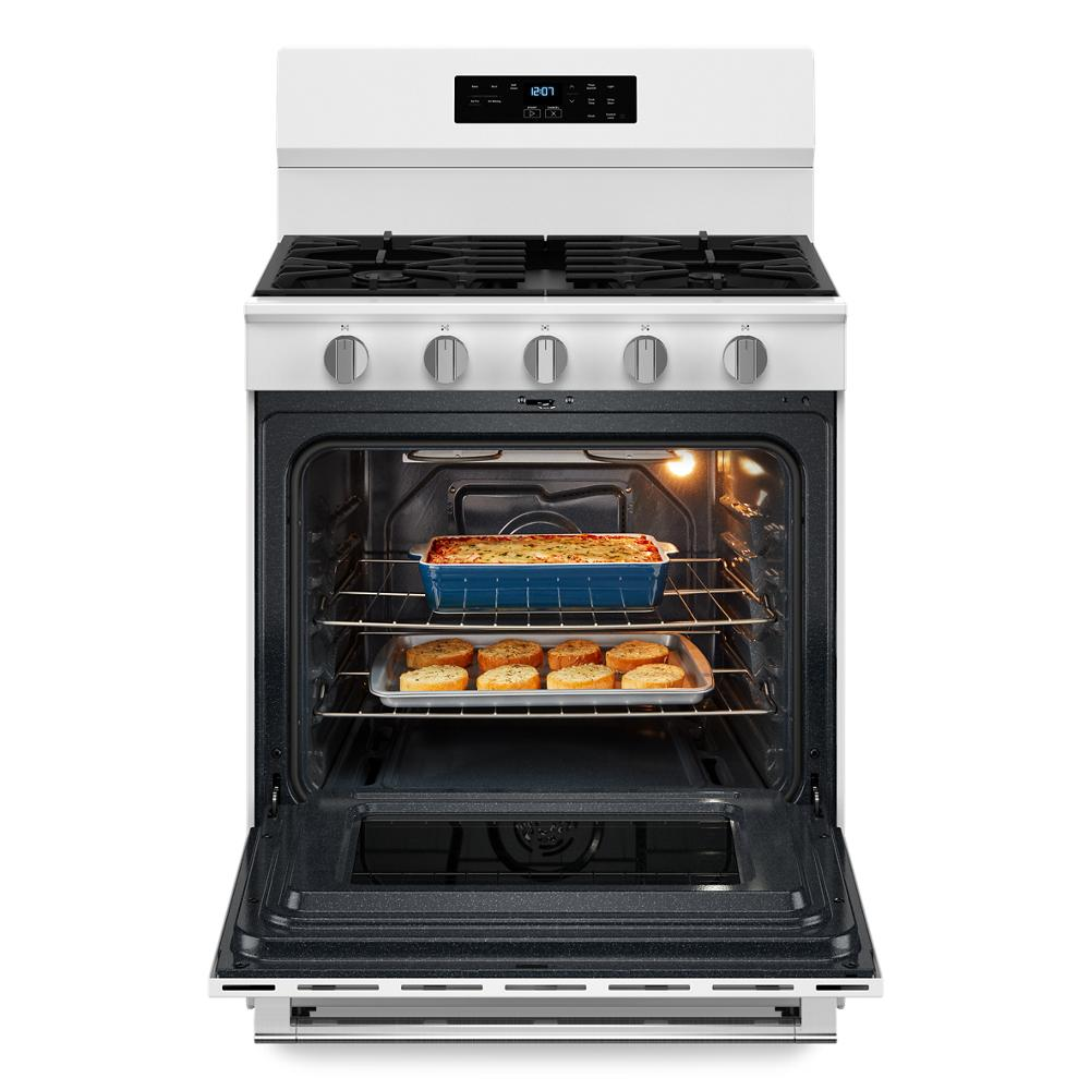 White 30-inch gas range with digital display, five burners, and oven open showing baked dishes inside from kitchen appliances collection