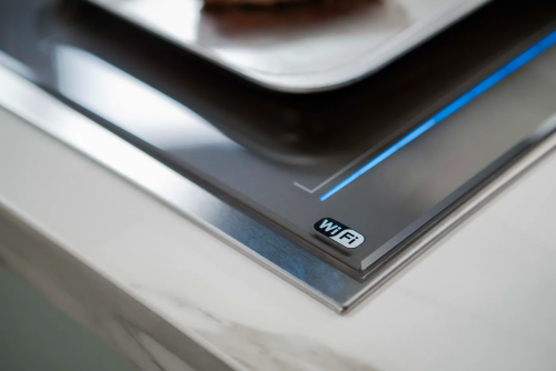 Close-up of dark gray induction cooktop corner with stainless steel frame and WiFi connectivity indicator light