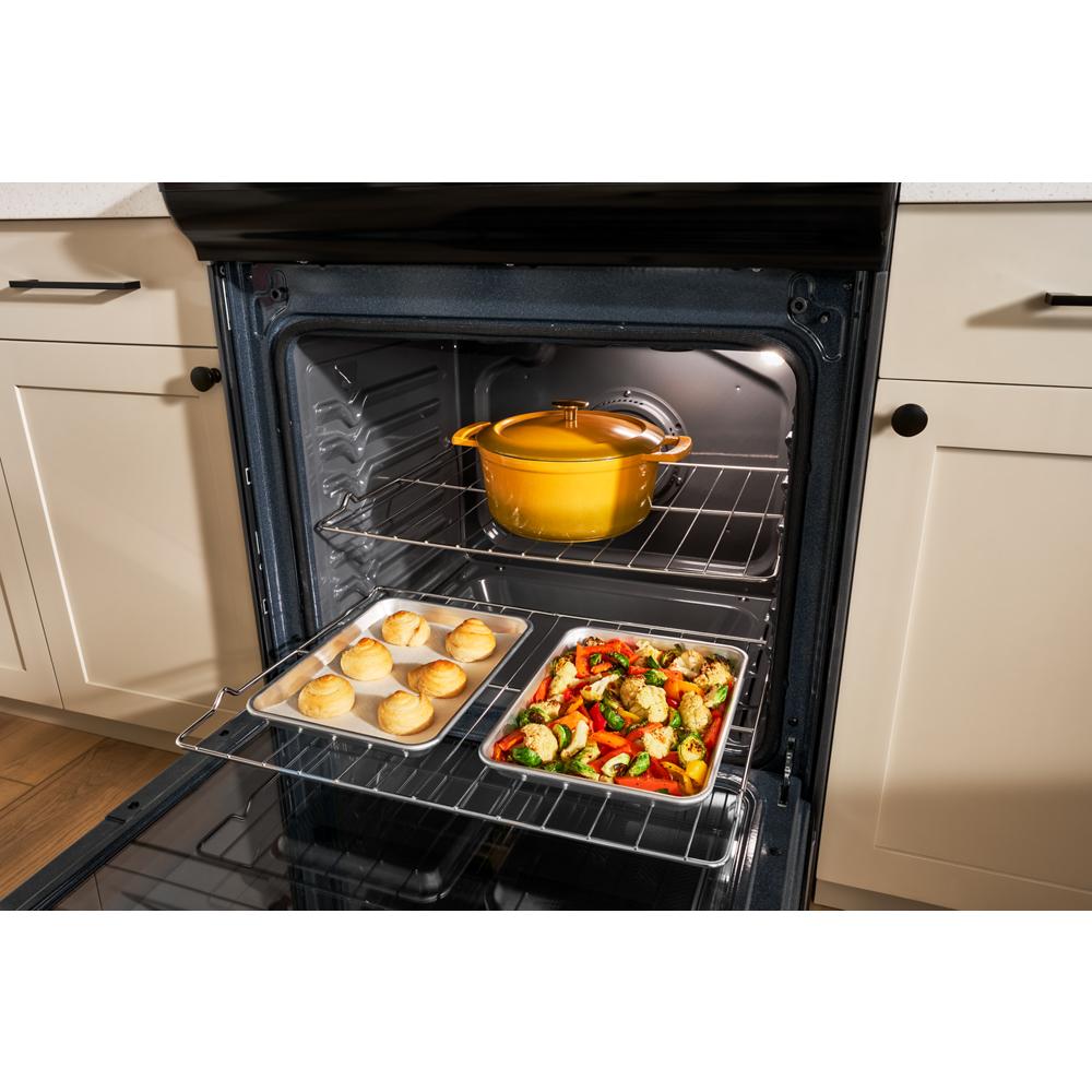 Open oven with two racks holding a yellow pot, baked rolls on a tray, and a sheet pan of roasted vegetables in kitchen setting