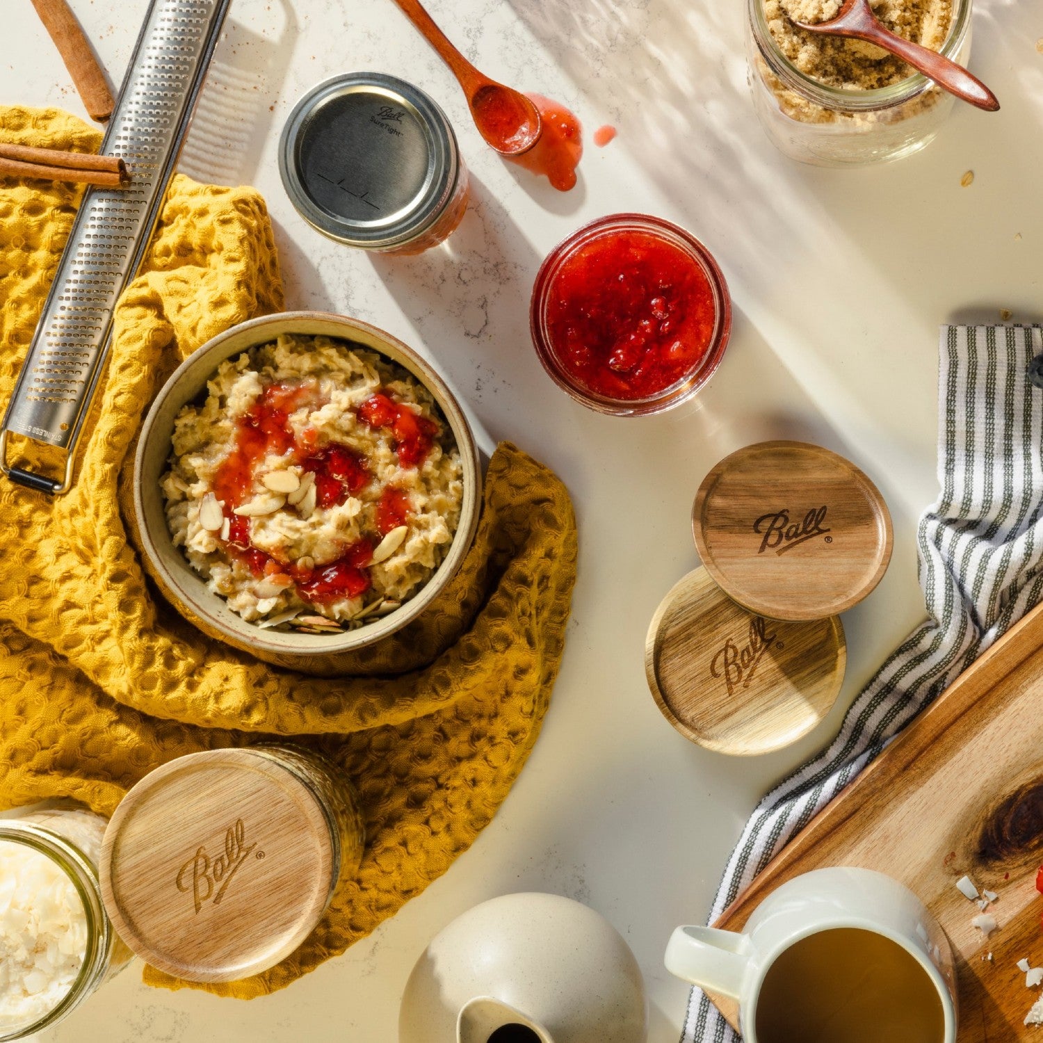 Three wooden wide mouth jar lids with Ball logo placed on a kitchen countertop with cooking utensils nearby