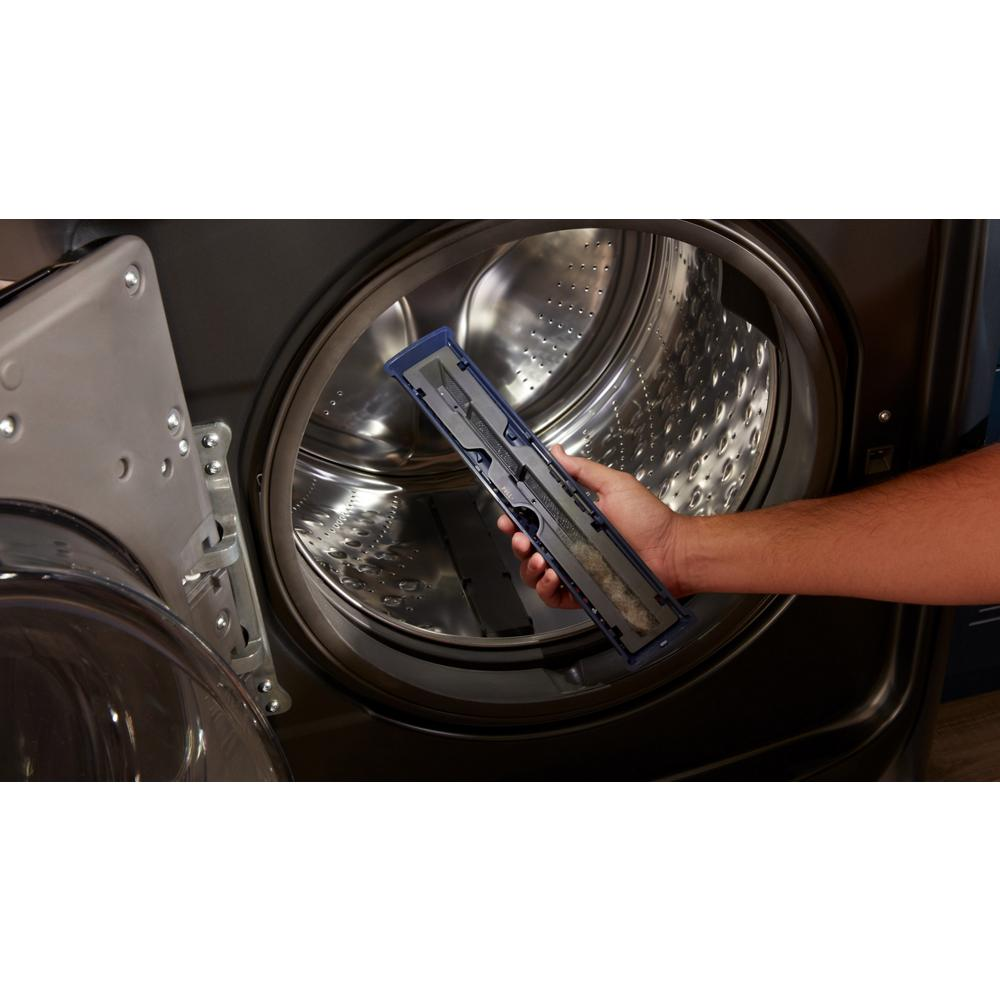 Hand holding Pet Pro filter removed from stainless steel drum of dark front load washer in home appliance setting