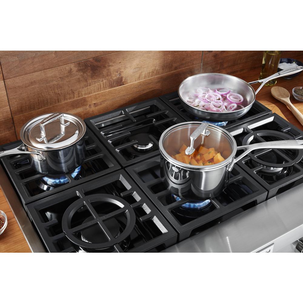 Close-up of stainless steel pots and frying pan cooking on a modern commercial-style gas rangetop in kitchenware collection