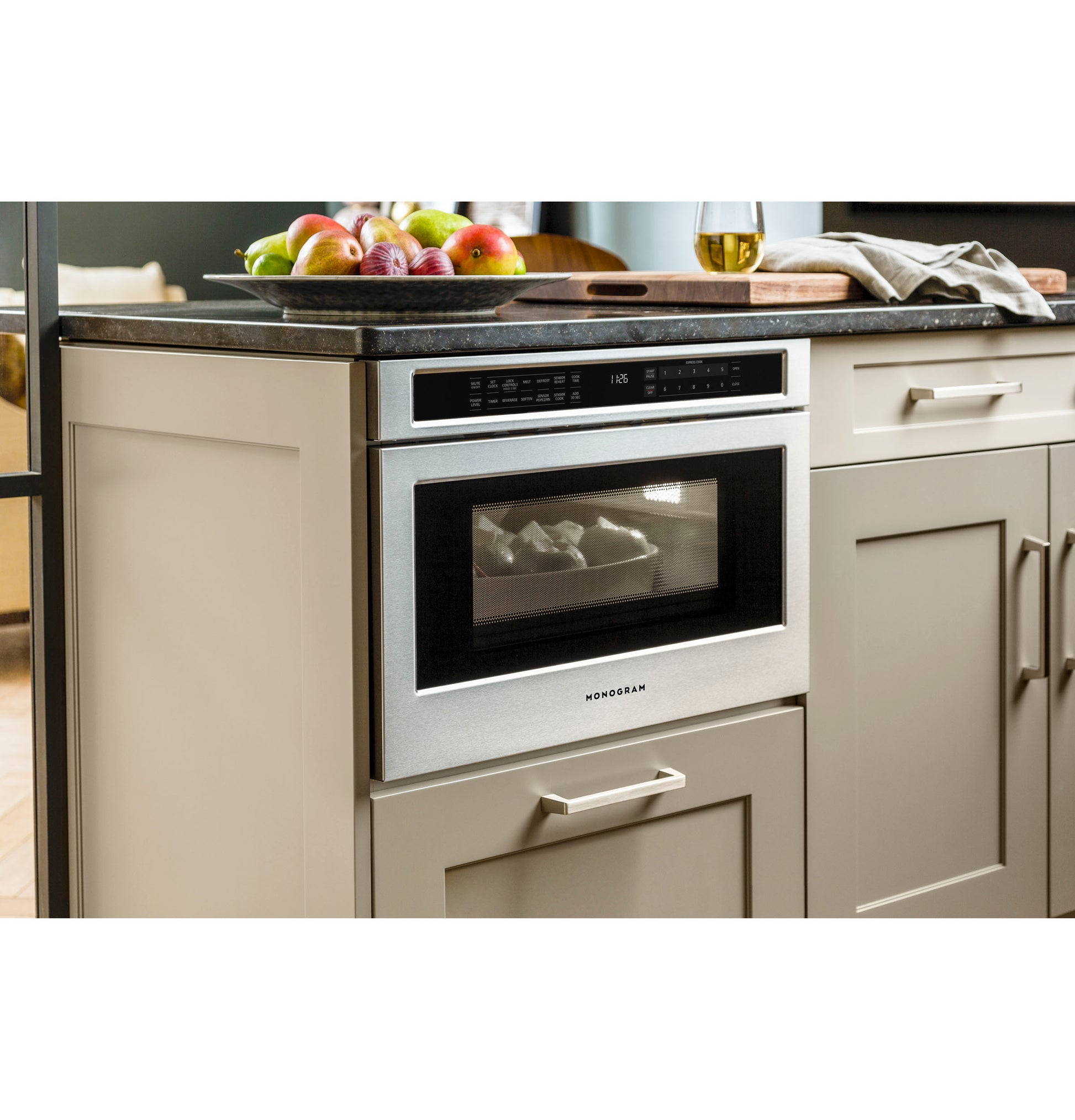 Built-in stainless steel microwave drawer integrated into beige kitchen cabinetry below dark countertop