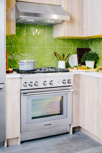 Stainless steel range with oven and matching custom insert hood set against green tiled backsplash in modern kitchen
