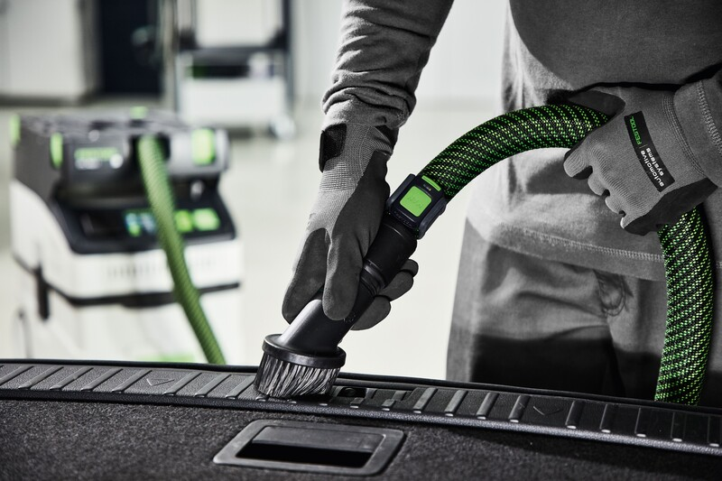 Handheld green and black plastic suction brush attachment cleaning a vehicle interior surface for home improvement tasks