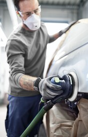 Person wearing protective mask using a random orbital sander on a car body in a workshop setting for tool accessories and home improvement