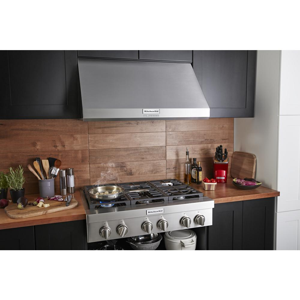Modern kitchen featuring stainless steel wall-mount canopy range hood above gas cooktop with utensils and spices nearby