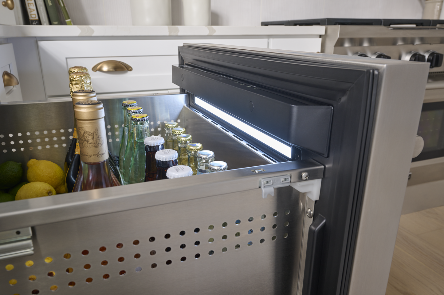Under-counter stainless steel refrigerator drawer open with chilled beverages in modern kitchen appliances collection