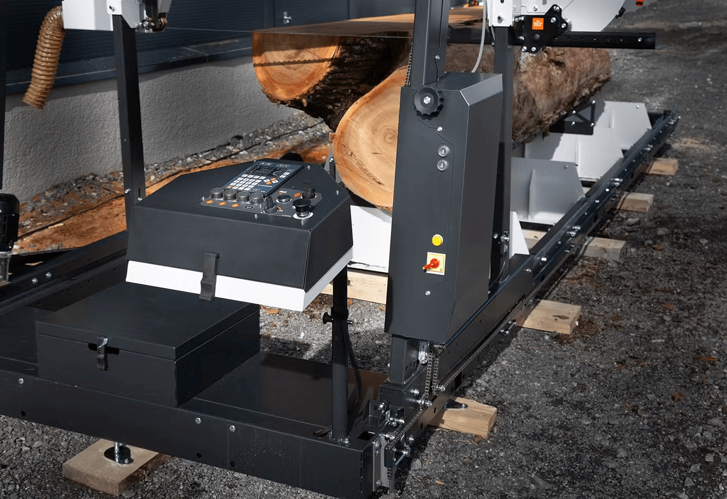 Close-up of a band sawmill cutting a large log into lumber with control panel and sturdy metal frame outdoors