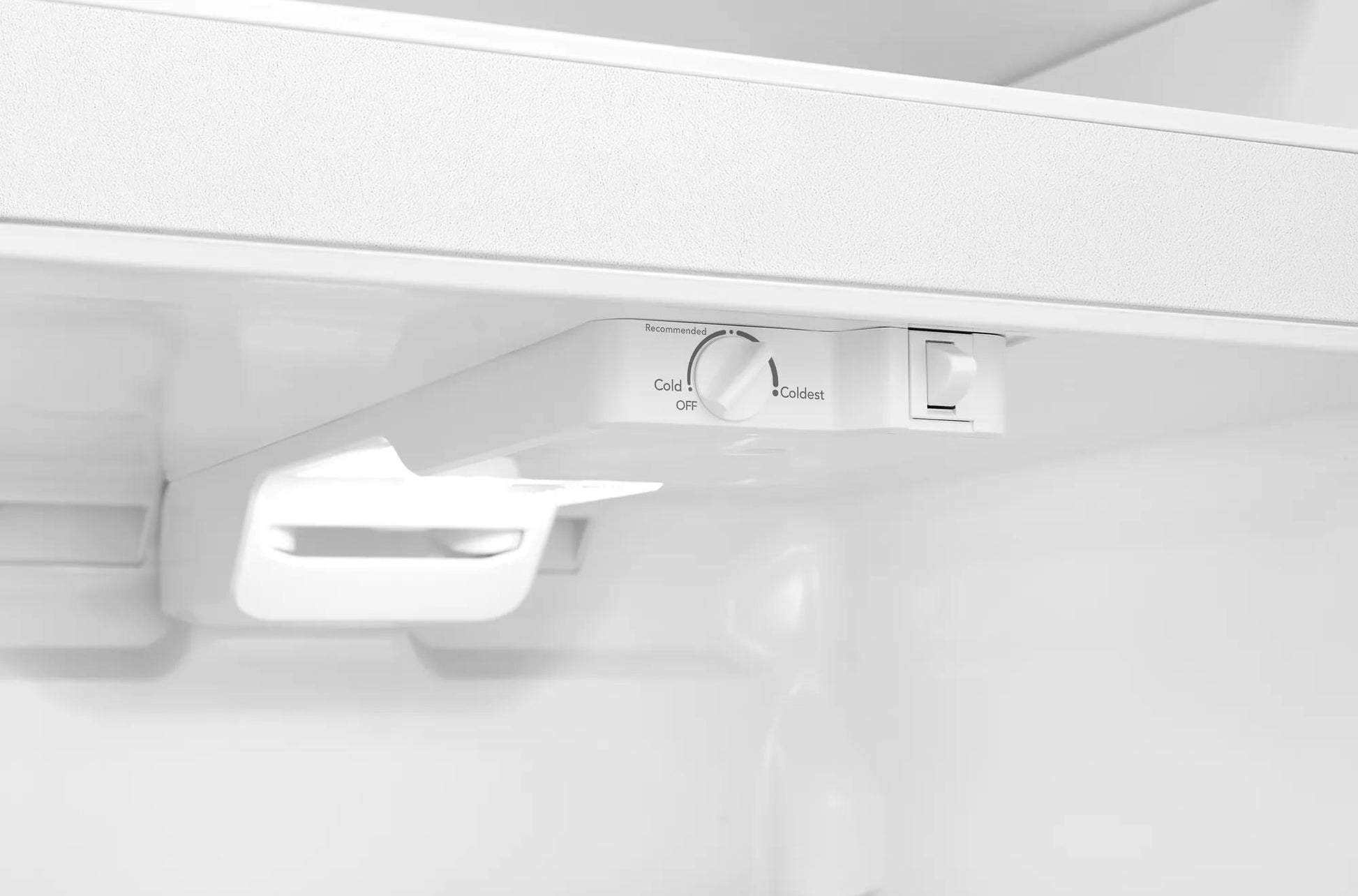 interior view of white top freezer refrigerator showing adjustable temperature control dial and light fixture in appliances collection