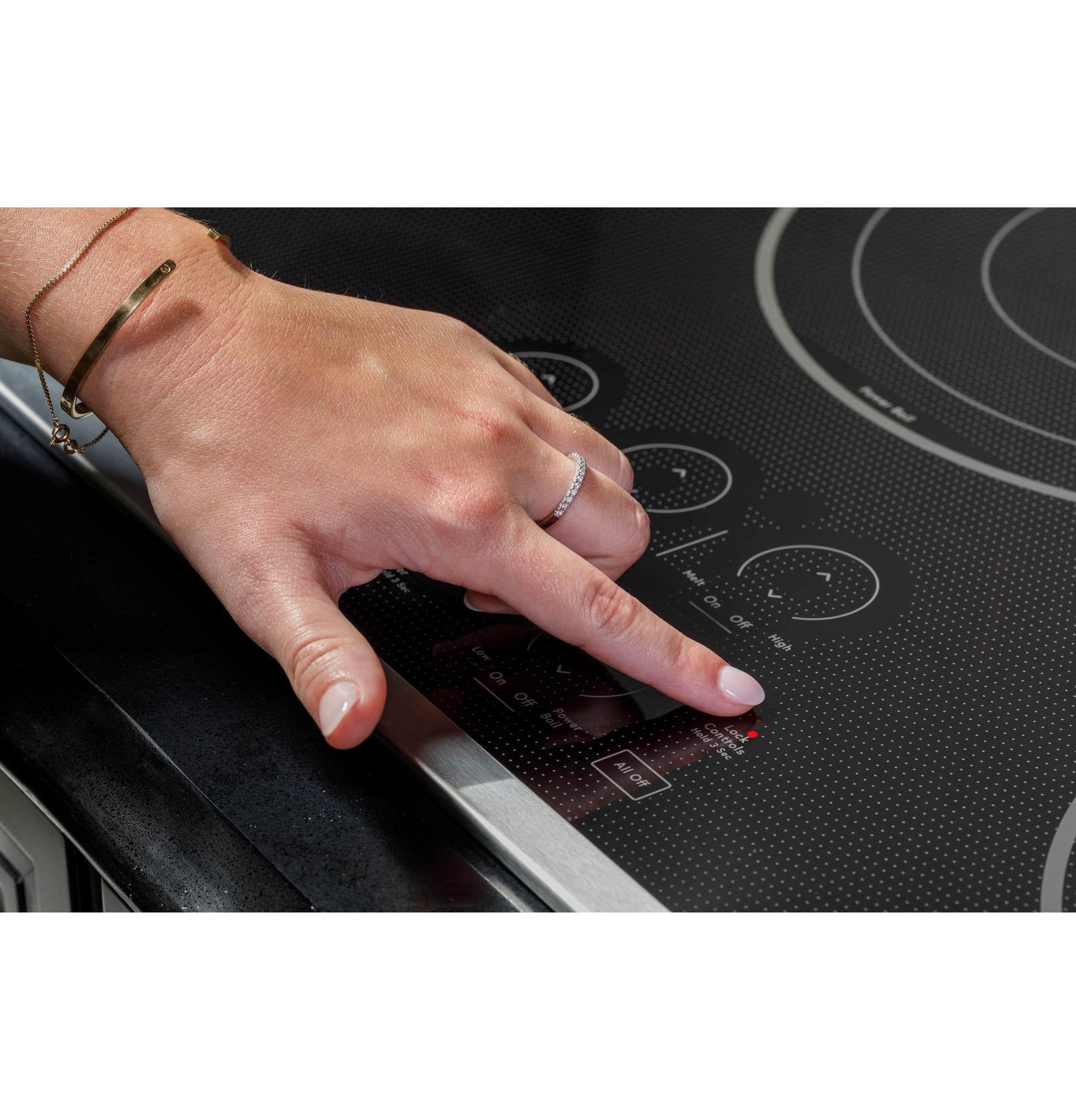 Hand pressing touch control on black glass electric cooktop in modern kitchen setting for home improvement
