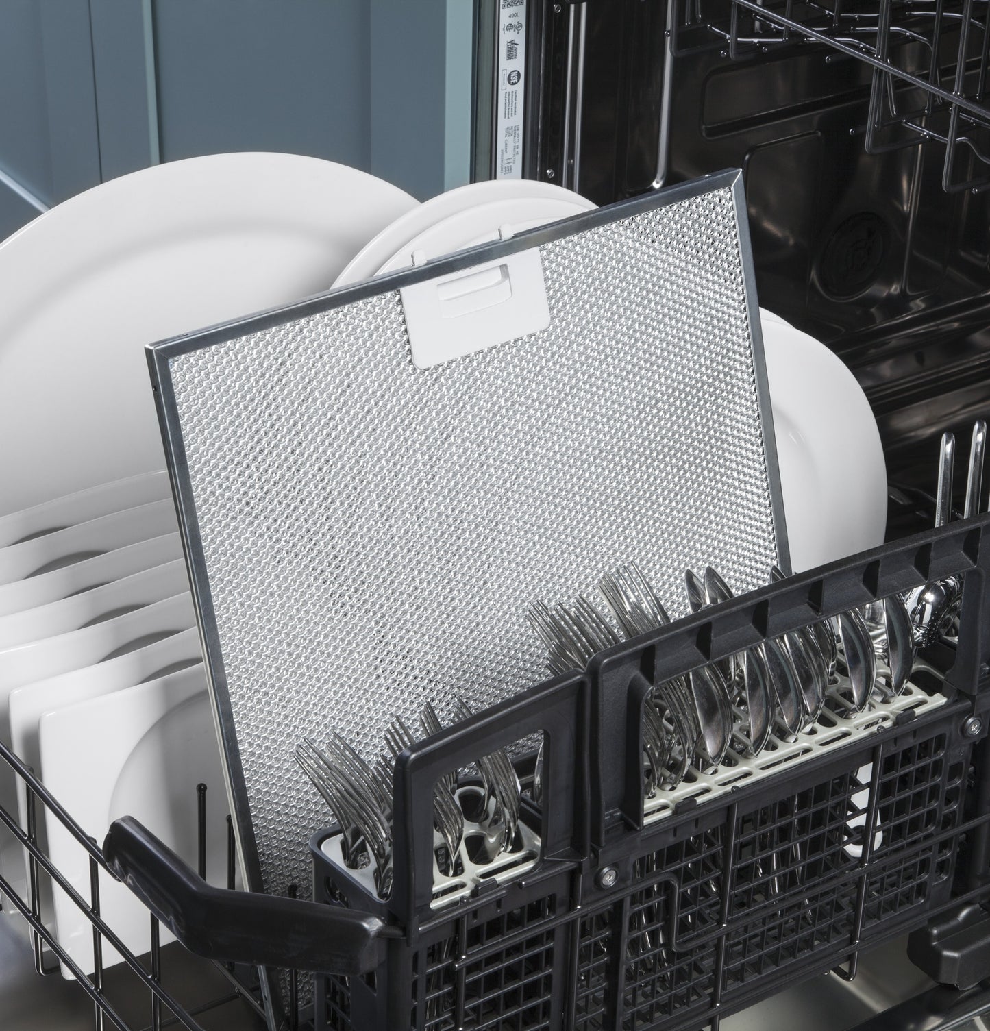 Open dishwasher loaded with white dishes, silverware, and a metal filter for kitchen and home appliances