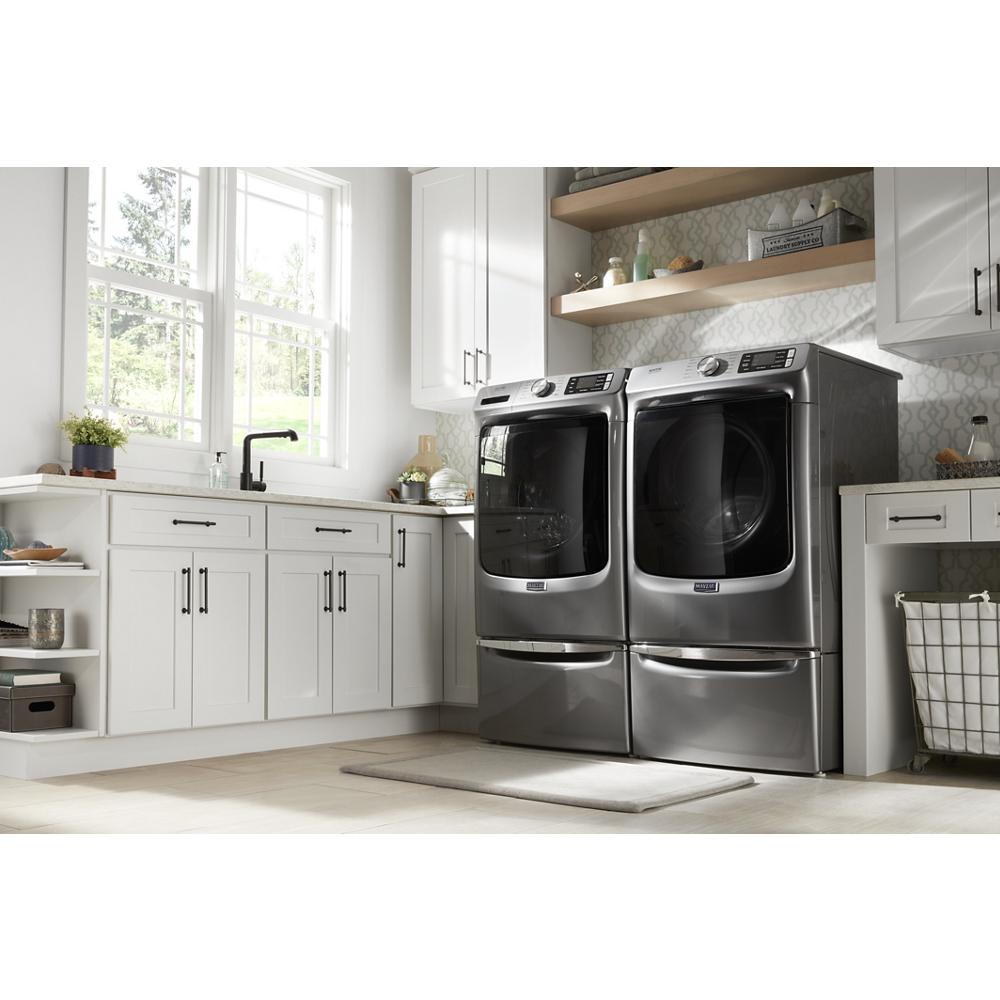 Laundry room with front load stainless steel washer and dryer on storage pedestals with white cabinetry and natural light