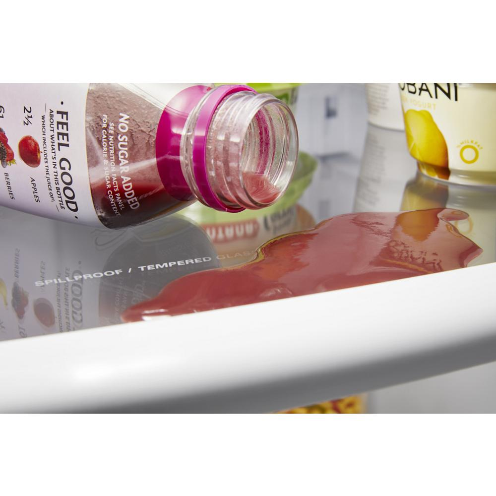 Close-up of a spillproof tempered glass refrigerator shelf with spilled juice and nearby beverage containers inside a kitchen appliance.